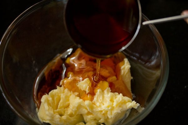 pouring kakvi syrup into bowl with butter for making eggless gingerbread cookies recipe.