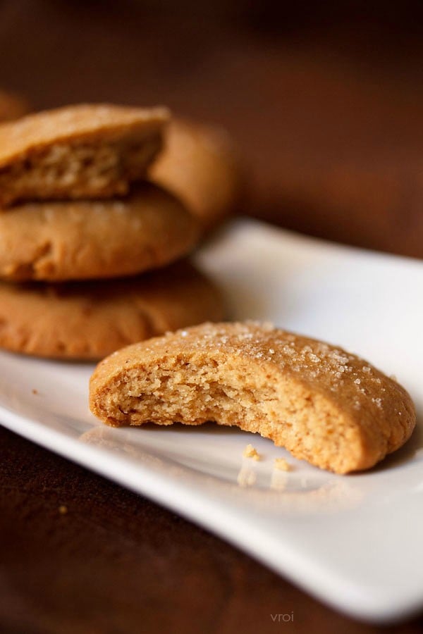 eggless gingerbread cookies stacked on a white plate with a close up of one with a bite taken out.