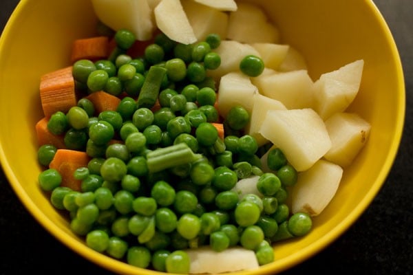 chopped potatoes, carrots, french beans and green peas in a yellow bowl to make veg kurma