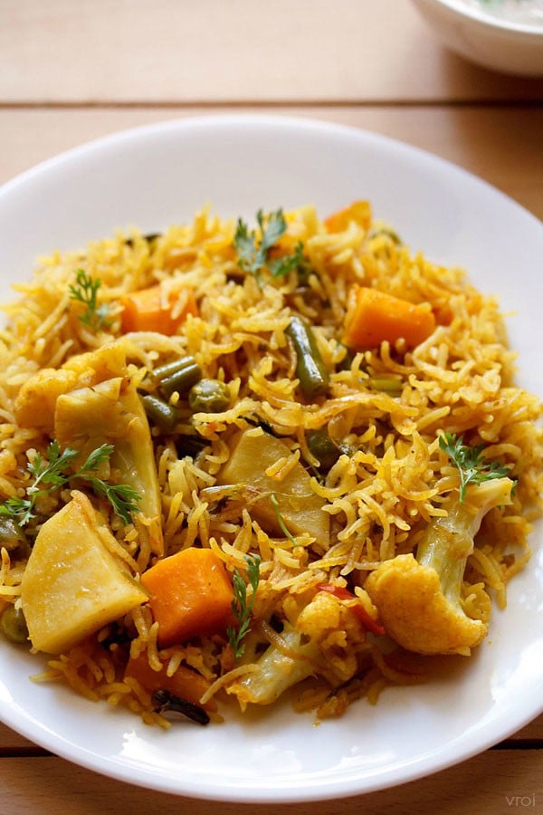 vegetable tahiri served on a white plate with a small bowl of raita kept on the top right side.