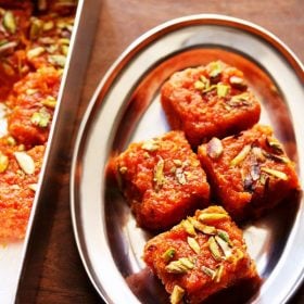 gajar ki barfi squares garnished with chopped pistachios and served on a steel plate with text layover.