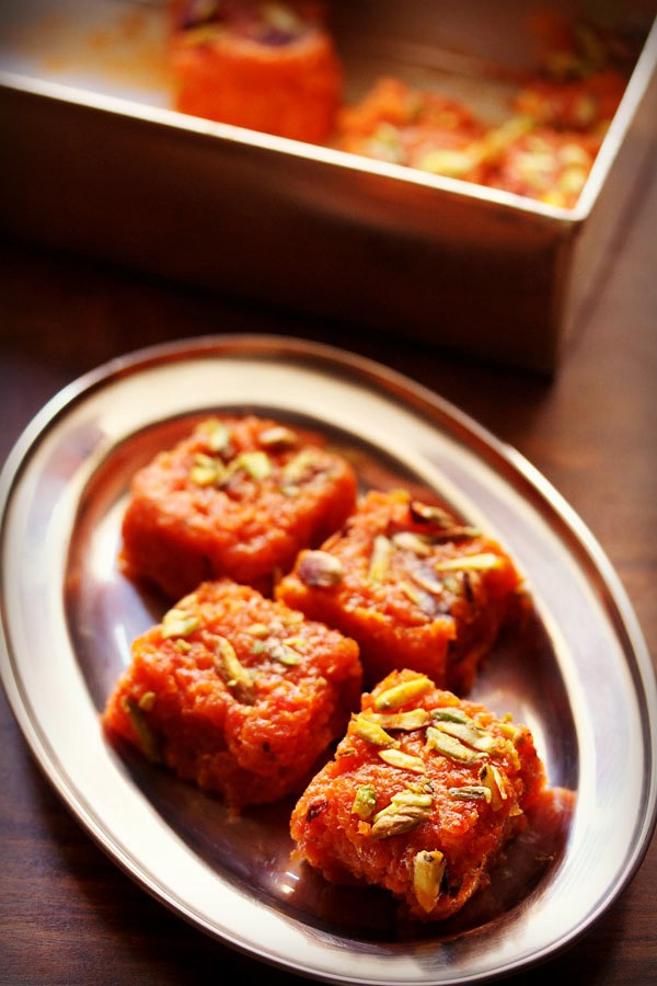 gajar ki barfi squares garnished with chopped pistachios and served on a steel plate.