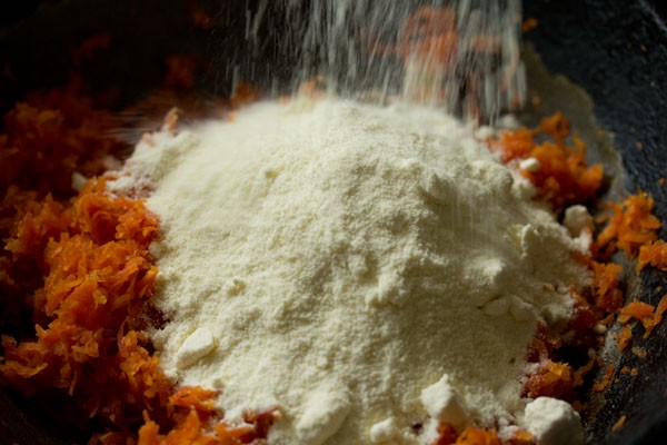 adding milk powder to grated carrot for making carrot burfi. 