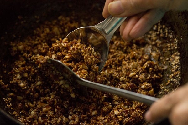 scooping the prepared mixture with a spoon to make til ke laddu. 