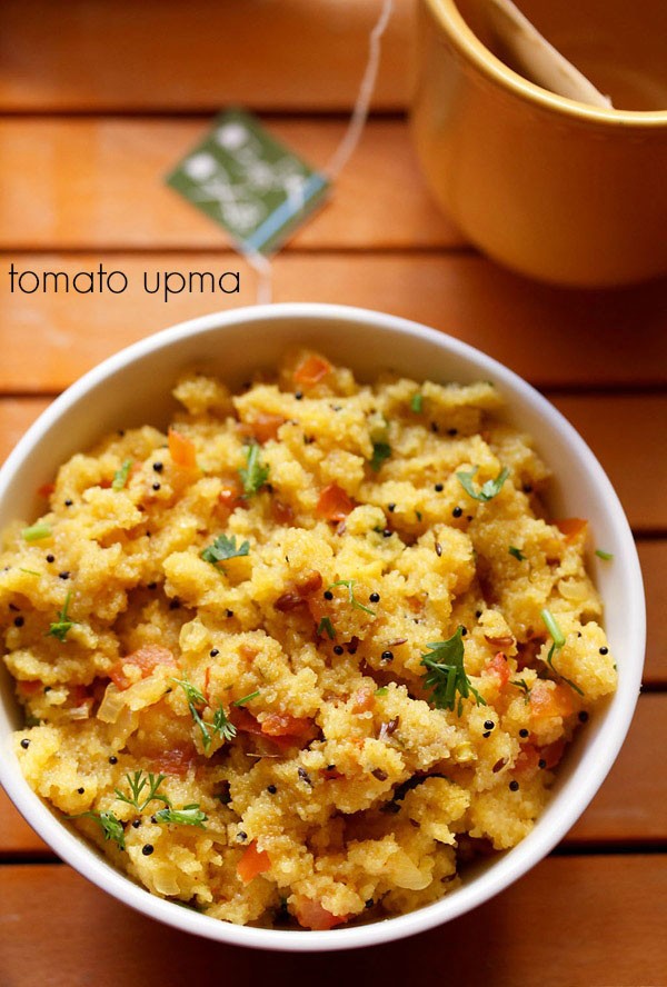 tomato upma garnished with coriander leaves and served in a bowl with a side of tea.