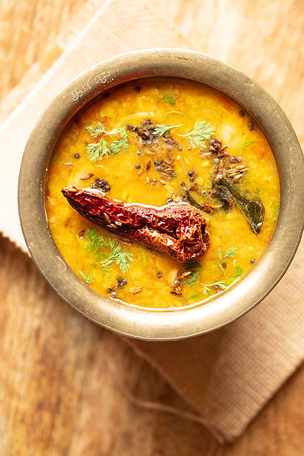 instant pot dal tadka served in a brass pot on a jute fabric on a brown wooden table