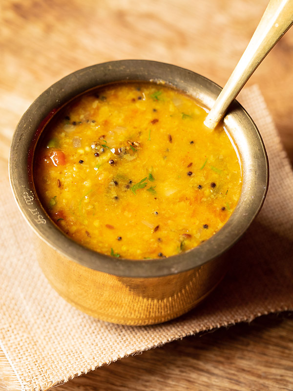 instant pot dal tadka served in a brass pot with a brass spoon inside the brass pot