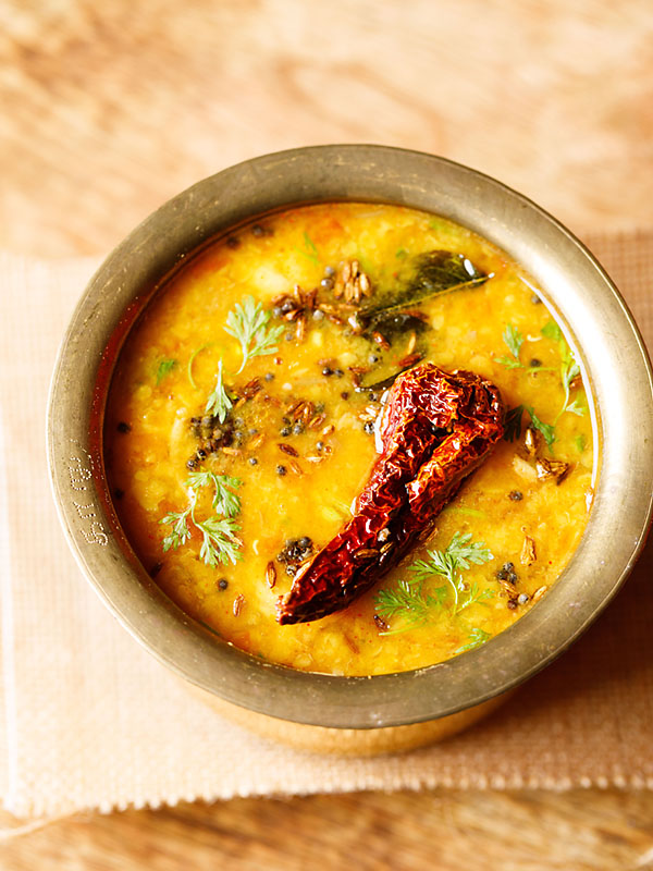 instant pot dal tadka served in a brass pot on a jute fabric on a brown wooden table