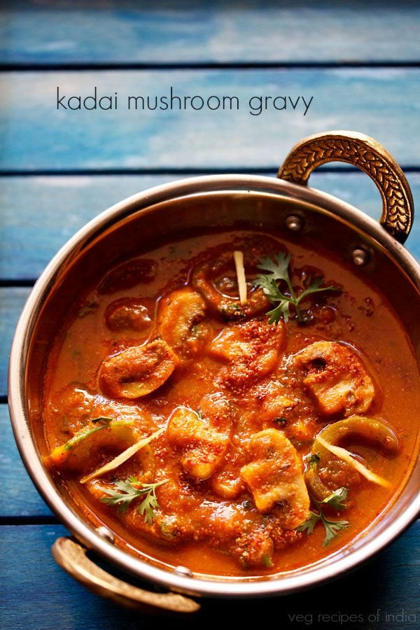 kadai mushroom gravy garnished with ginger julienne and cilantro served in a kadai on a blue board