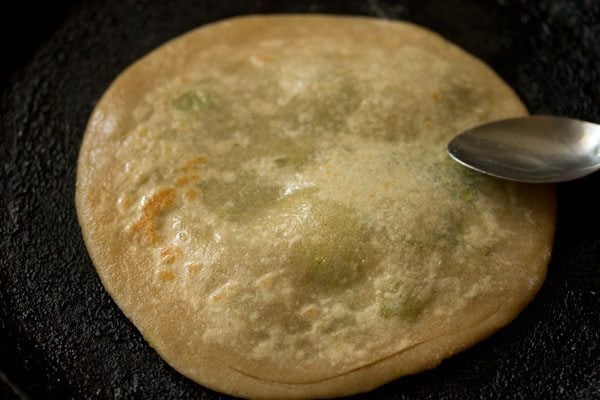 spreading ghee on second side of peas paratha