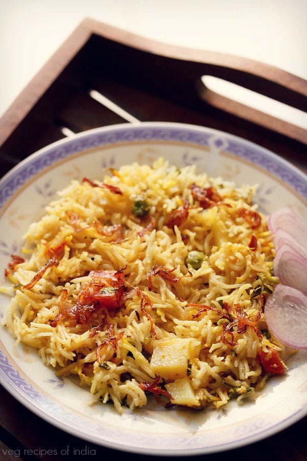 pressure cooker biryani served on a plate with a side of sliced onions. 