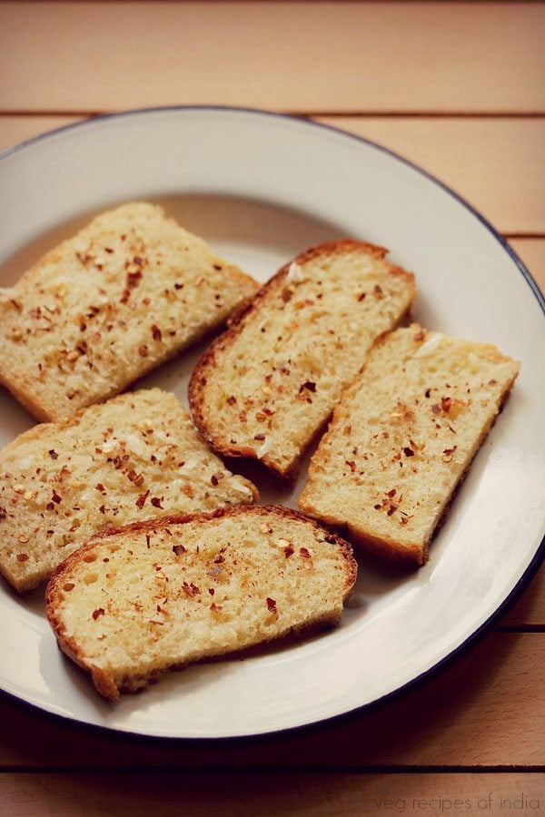 garlic bread toast sprinkled with red chili flakes, dried oregano and served on a plate. 