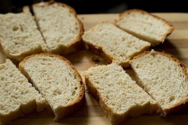 halved bread slices on a chopping board for garlic bread recipe. 