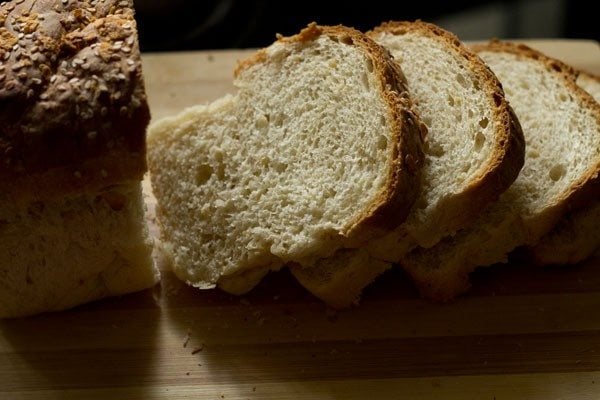 loaf of bread cut into slices on a chopping board for garlic bread recipe. 