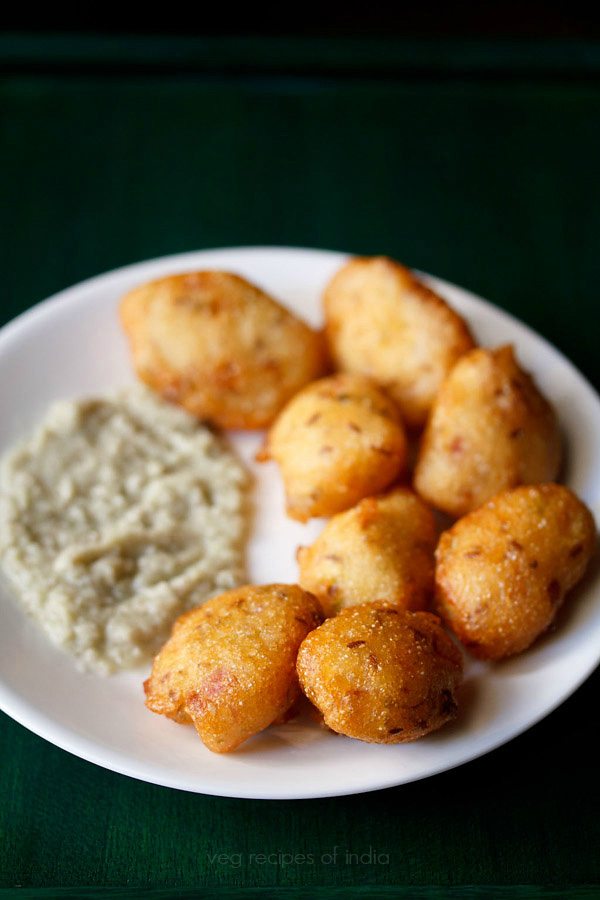 round white plate filled with Andhra punugulu fritters and a swoosh of peanut chutney on a black table.