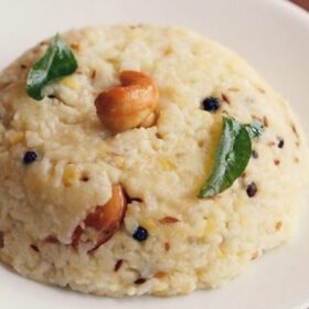 ven pongal garnished with a cashew and curry leaves and served on a white plate.