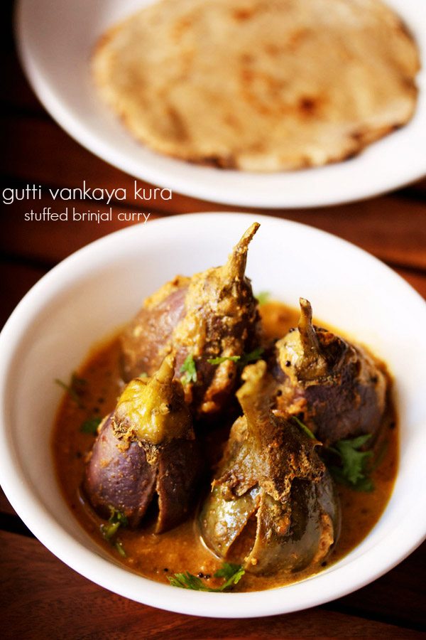 gutti vankaya garnished with coriander leaves and served in a white bowl with a plate of chapatis kept in the background and text layover.