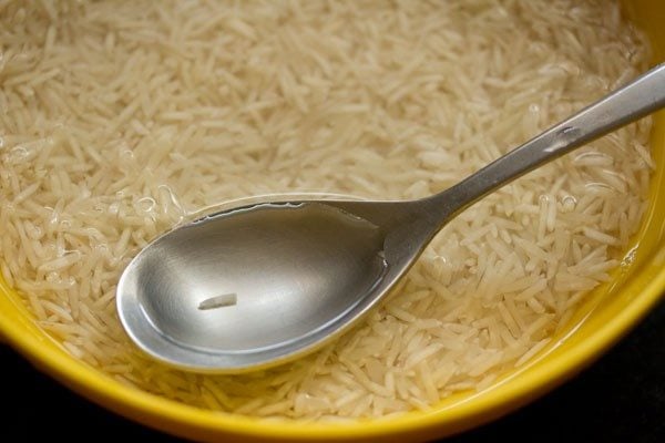 basmati rice and water in a bowl with a spoon in yellow bowl showing clear water.