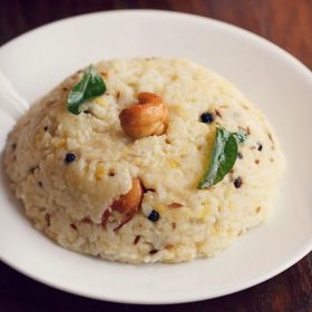 ven pongal garnished with a cashew and curry leaves and served on a white plate.