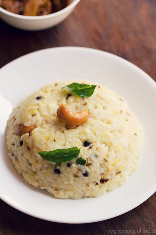 pongal garnished with a cashew and curry leaves and served in a white plate