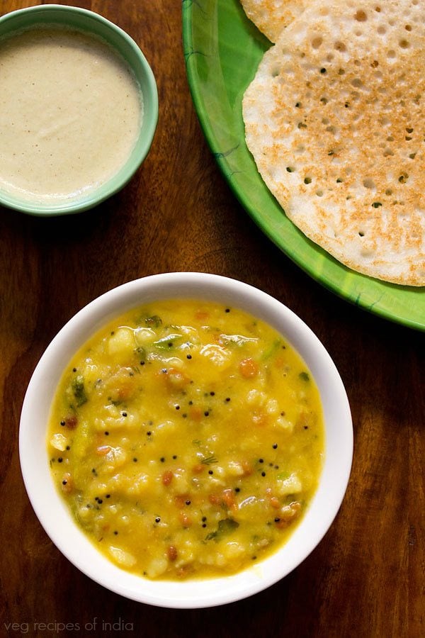 top shot of potato sagu served in a white bowl with a plate of dosas and a small bowl of coconut chutney. 