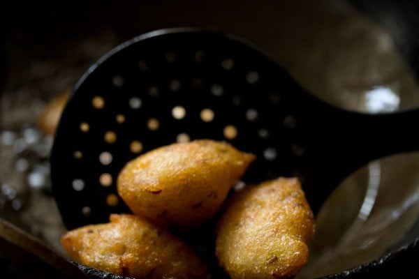 removing fried punugulu from the oil with a slotted spoon.