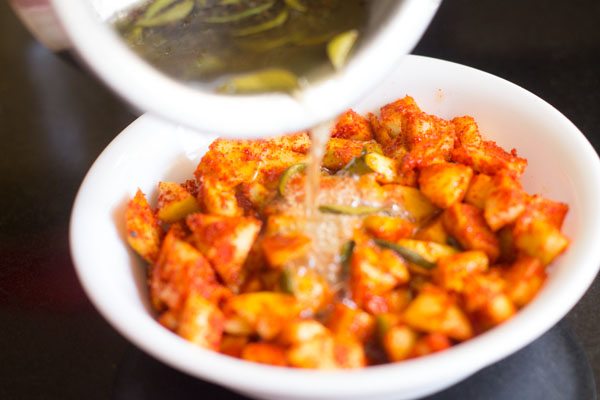 hot oil and spices mixture being added to mango cubes in the heat-proof bowl for the instant mango pickle.  