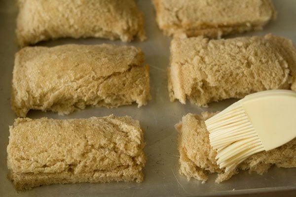 lightly brushing prepared paneer bread rolls kept on a baking tray with some oil. 