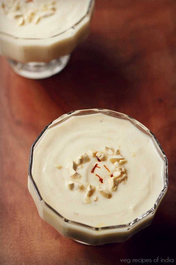 greek yogurt shrikhand topped with chopped cashews and a few saffron strands in a glass bowls on brown wooden board
