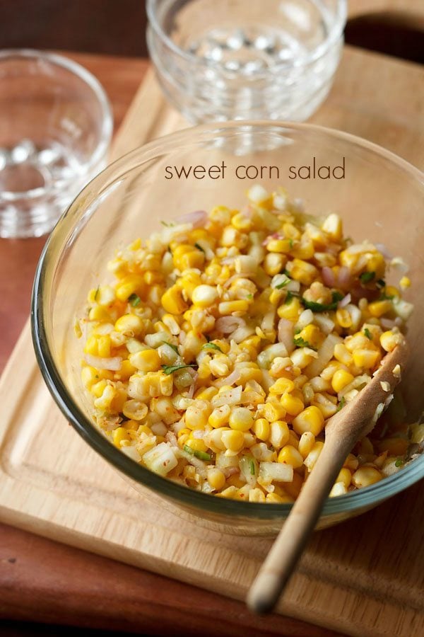 corn salad served in a glass bowl with a wooden spoon in it and text layover.