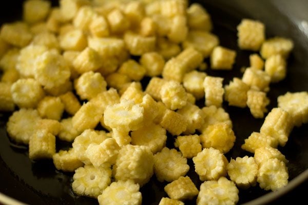 sliced baby corn added in hot olive oil in pan.