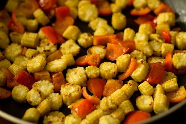 sautéing baby corn and red bell pepper in the pan.