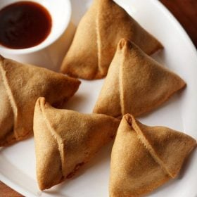 baked samosa served with tamarind chutney on a white platter.