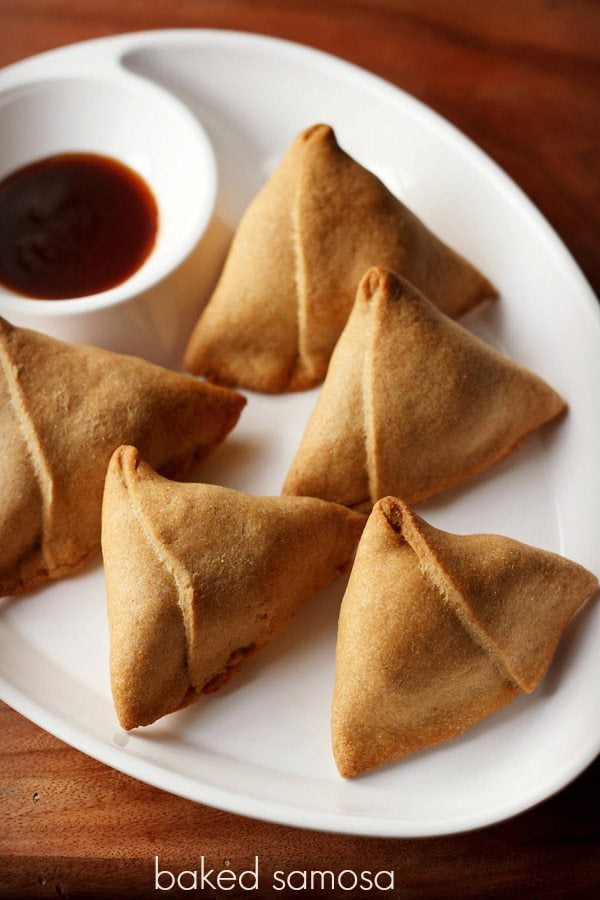 baked samosa served with tamarind chutney on a white platter.