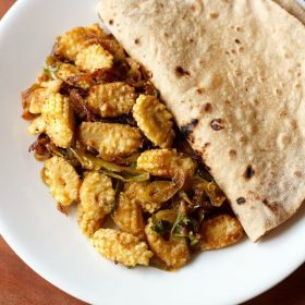 baby corn sabji served on a white plate with folded chapati by the side.