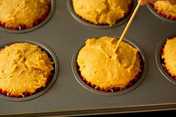 checking the doneness of the mango muffins using a toothpick. 