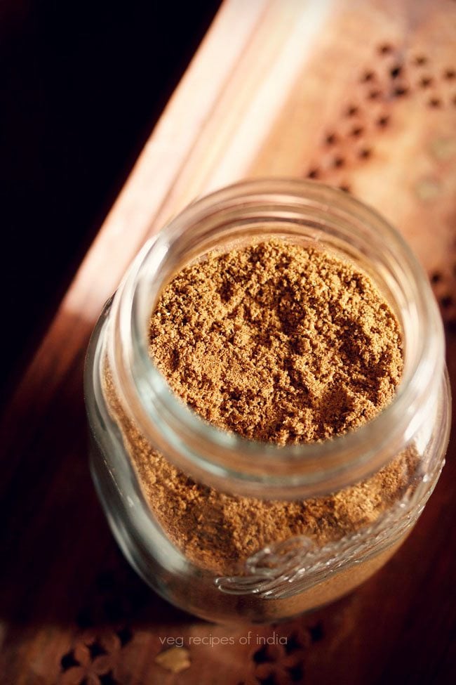 garam masala in a glass  jar on a brown wooden tray.