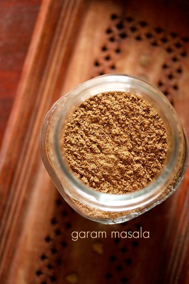 garam masala powder in a glass  jar on a brown wooden tray.