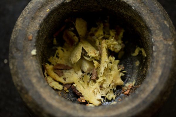 Crushed cardamom, green cardamoms, cloves and ginger in a mortar.