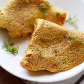 oats chilla garnished with coriander sprigs and served folded in a triangle on a white plate.