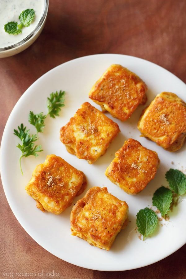 amritsari paneer garnished with coriander sprigs, mint leaves and served on a white colored plate with text layover.