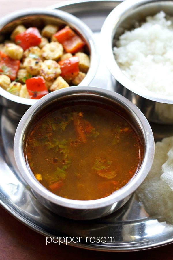 milagu rasam served in a steel bowl on a plate with a bowl of vegetable stir fry and steamed rice with text layover. 