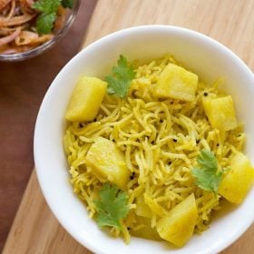 potato rice garnished with coriander leaves and served on a white plate with a side of onion salad.