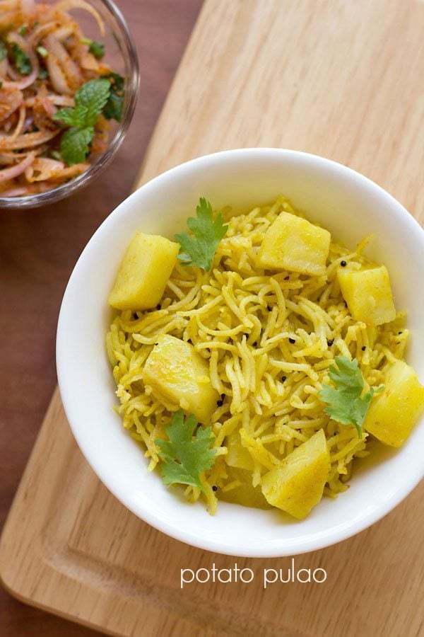 potato rice garnished with coriander leaves and served on a white plate with a side of onion salad.