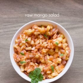 raw mango salad garnished with a mint sprig and served in a white bowl with text layovers.