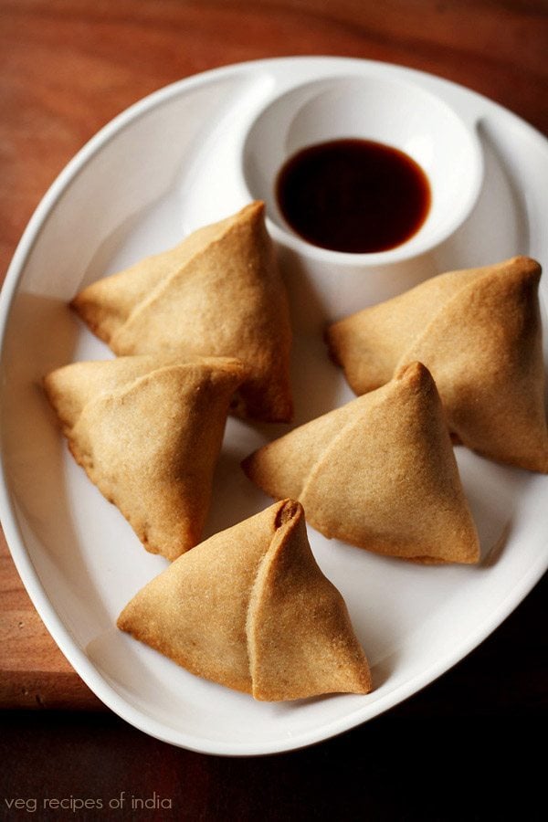 baked samosas served with tamarind chutney on a white plate. 