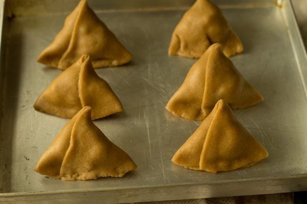 prepared samosas placed on a baking tray. 