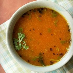 tomato charu with a coriander leaf in a light green ceramic bowl on a light green-blue-white checkered napkin