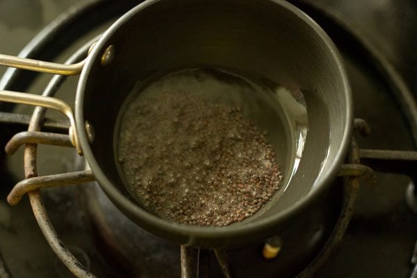 mustard seeds crackling in oil in a small black tadka pan