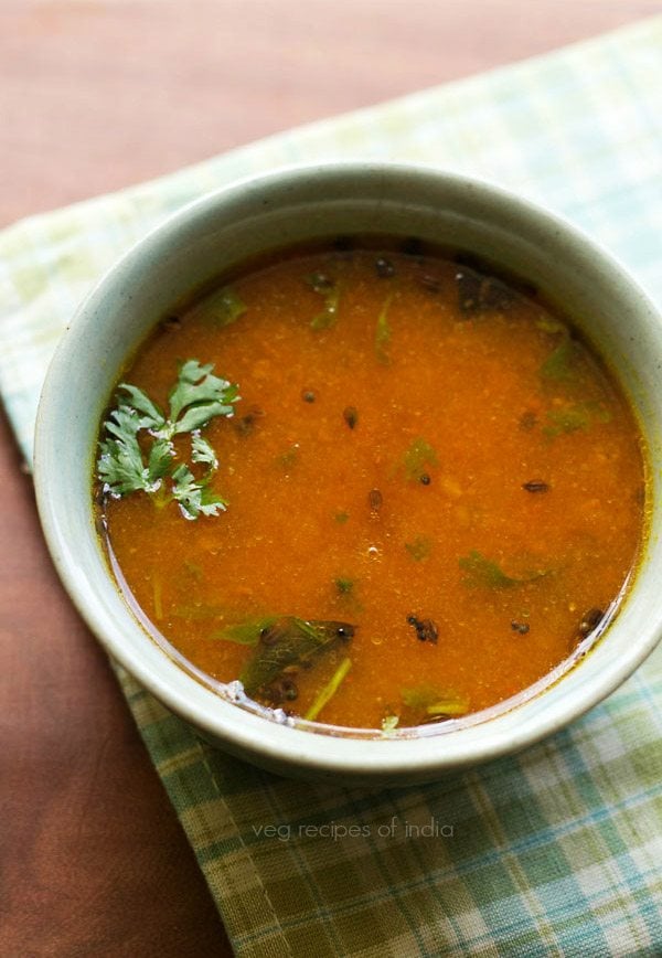 tomato charu with a coriander leaf in a light green ceramic bowl on a light green-blue-white checkered napkin